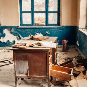 A deserted classroom showing an old desk and scattered papers in a dilapidated setting.