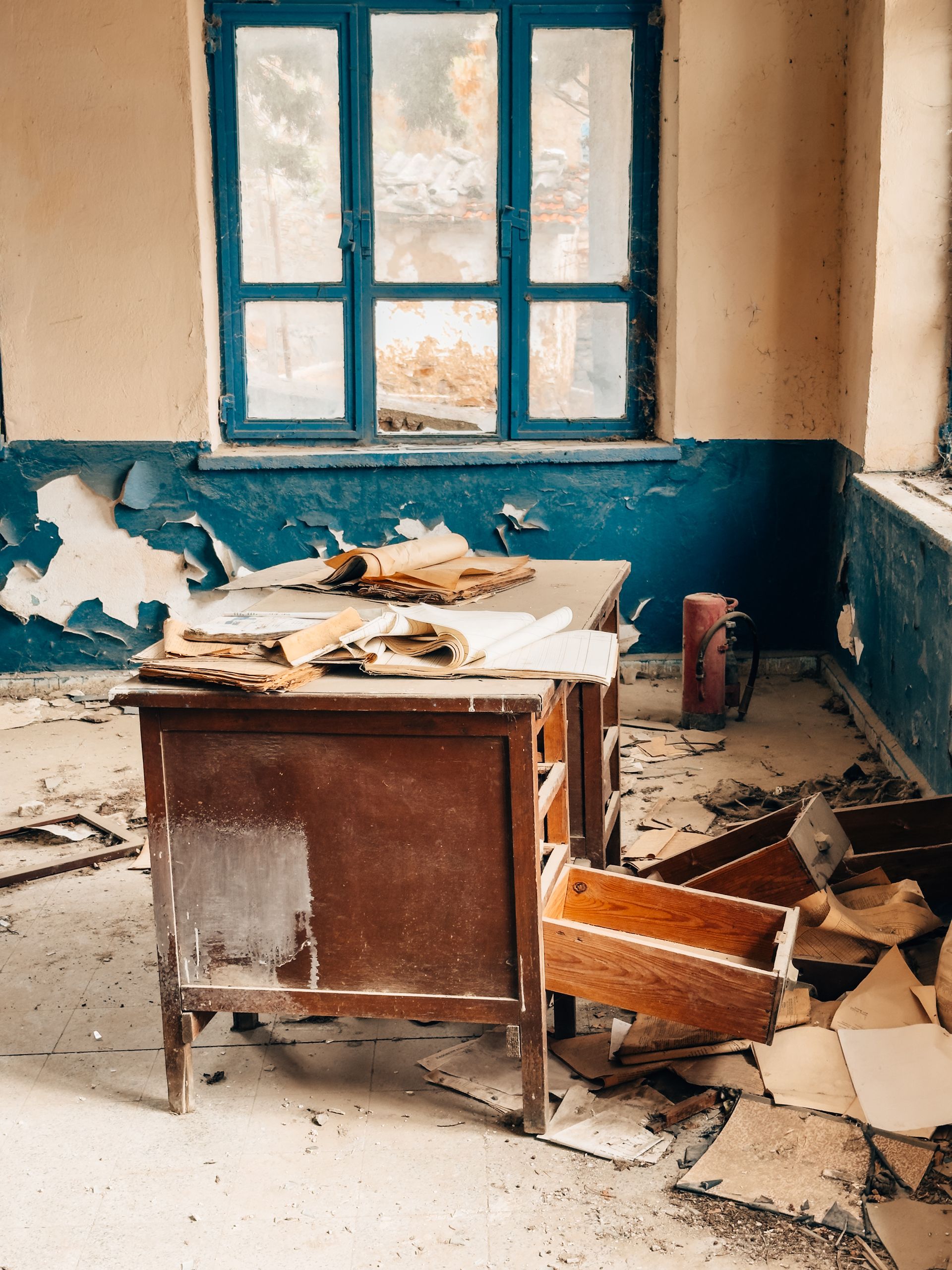 A deserted classroom showing an old desk and scattered papers in a dilapidated setting.